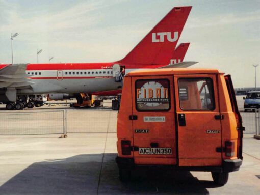 Orangenes FIDAN Auto vor einem LTU Flugzeug am Flughafen